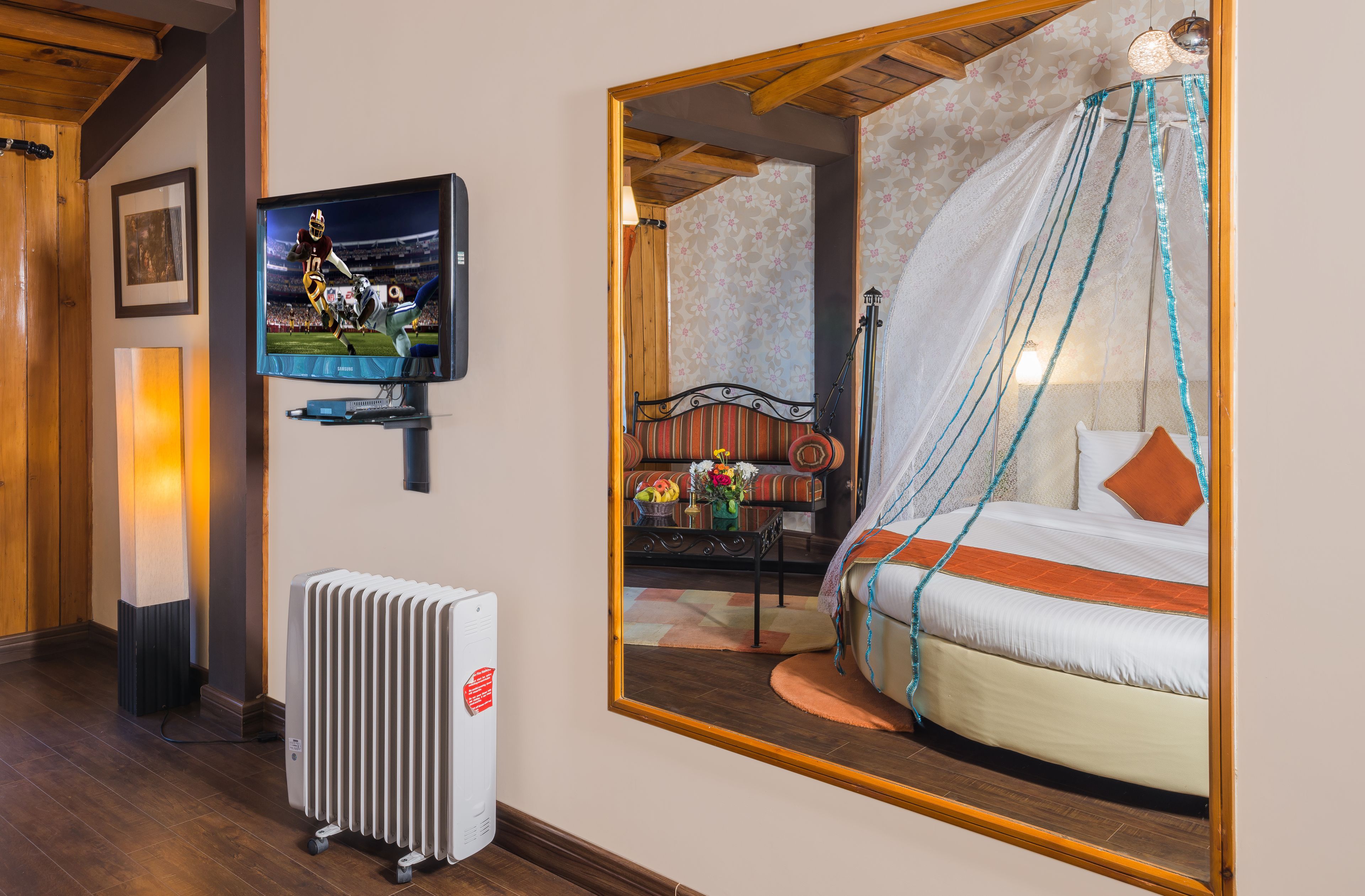 Ett hotellrum med en stor säng, en tv, ett element och en spegel som reflekterar rummet.