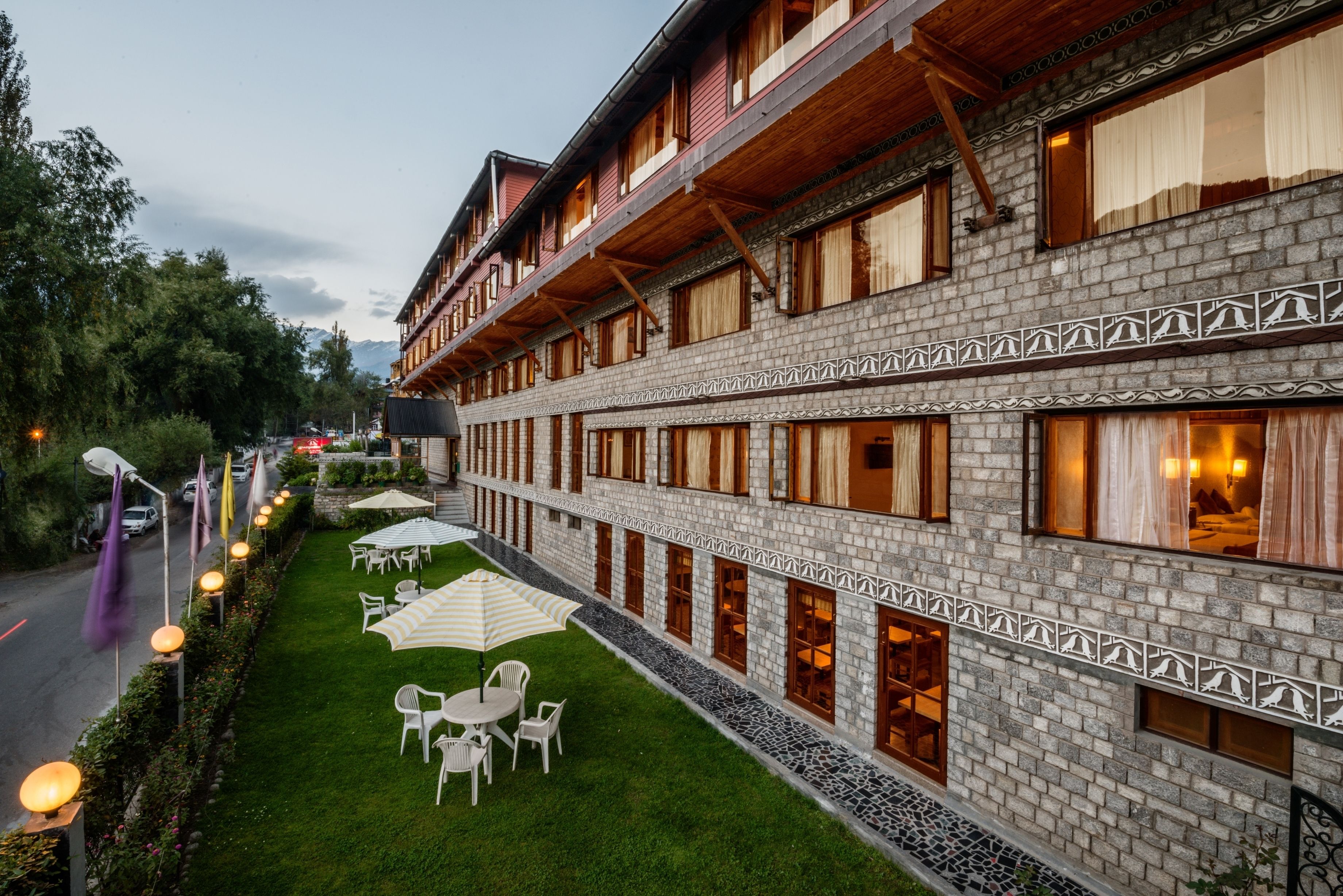 Un hôtel à plusieurs étages, doté d’une façade en briques, d’un espace extérieur aménagé pour s’asseoir et d’une pelouse bien entretenue.
