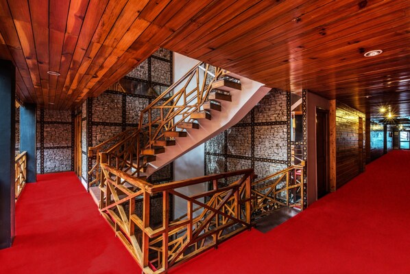 A spiral staircase with wooden railings in a room with stone walls and a red carpet. - Honeymoon Inn (Manali)