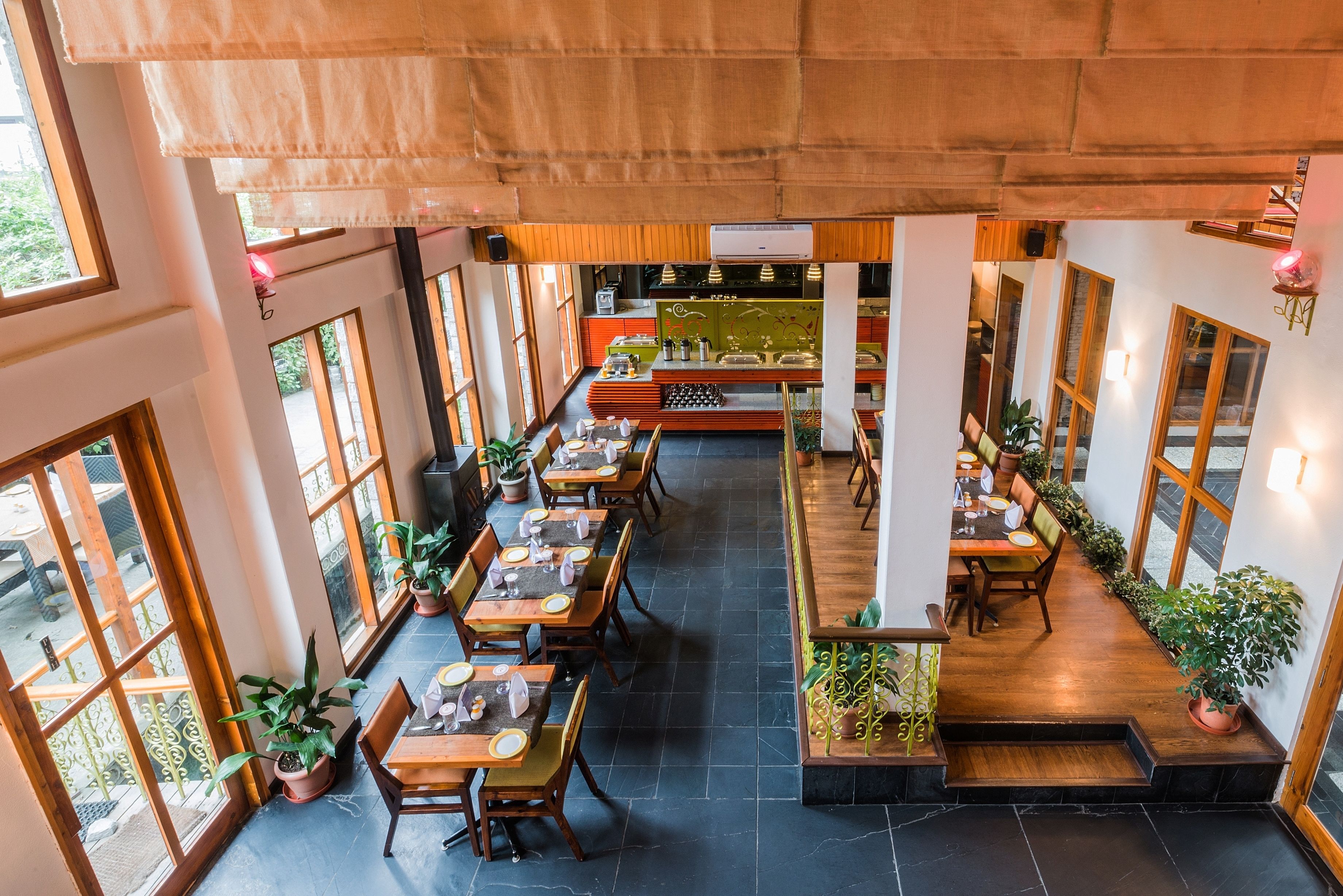 Un restaurant doté de nombreuses tables et chaises, de plantes en pot et d’un plafond en bois.