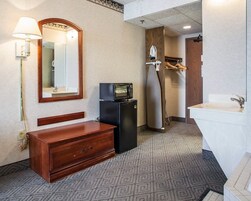 Un baño de hotel con tocador de madera, microondas, refrigerador, lavamanos y espejo.