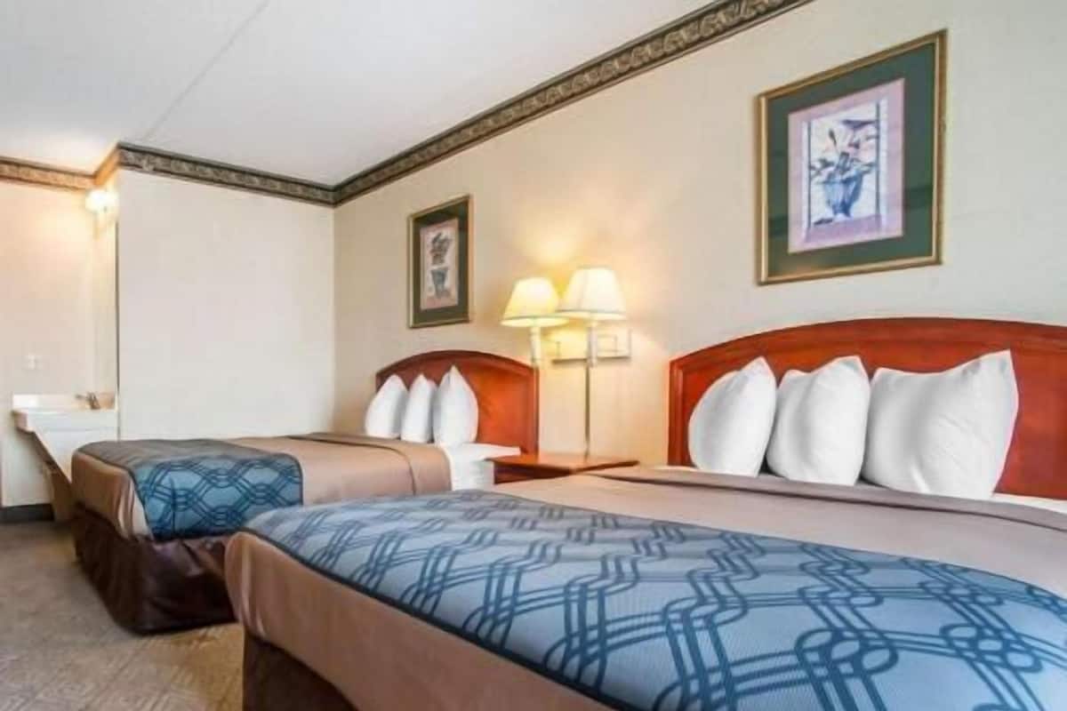 Une chambre d’hôtel avec deux lits, une table de chevet, une lampe et un tableau encadré au mur.