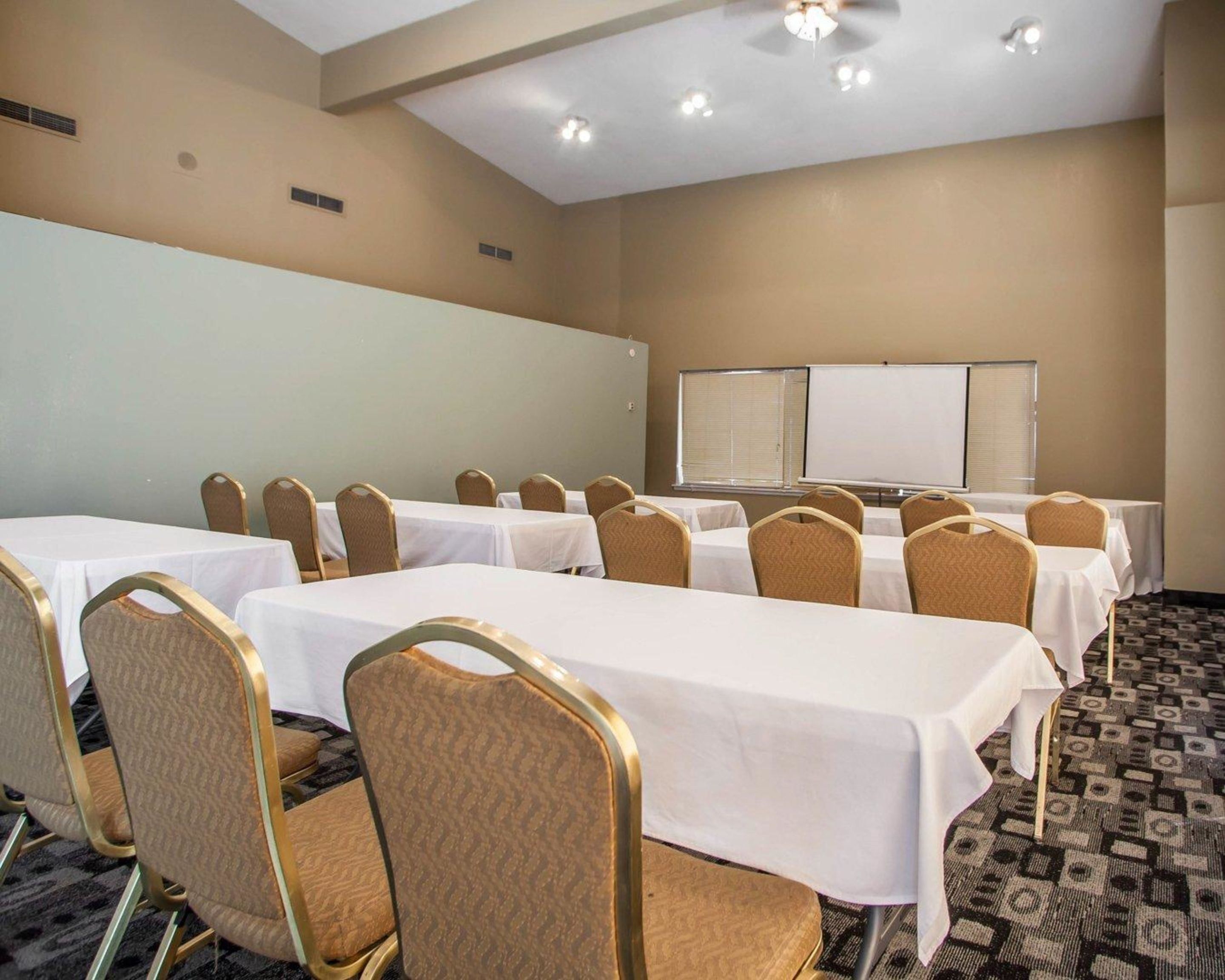 Sala de conferências com mesas, cadeiras, quadro branco e tela de projeção.