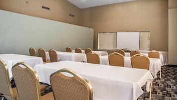 Sala de conferências com mesas, cadeiras, quadro branco e tela de projeção.