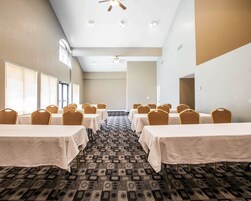 Un salón de conferencias con varias mesas y sillas, alfombra estampada y ventiladores de techo.