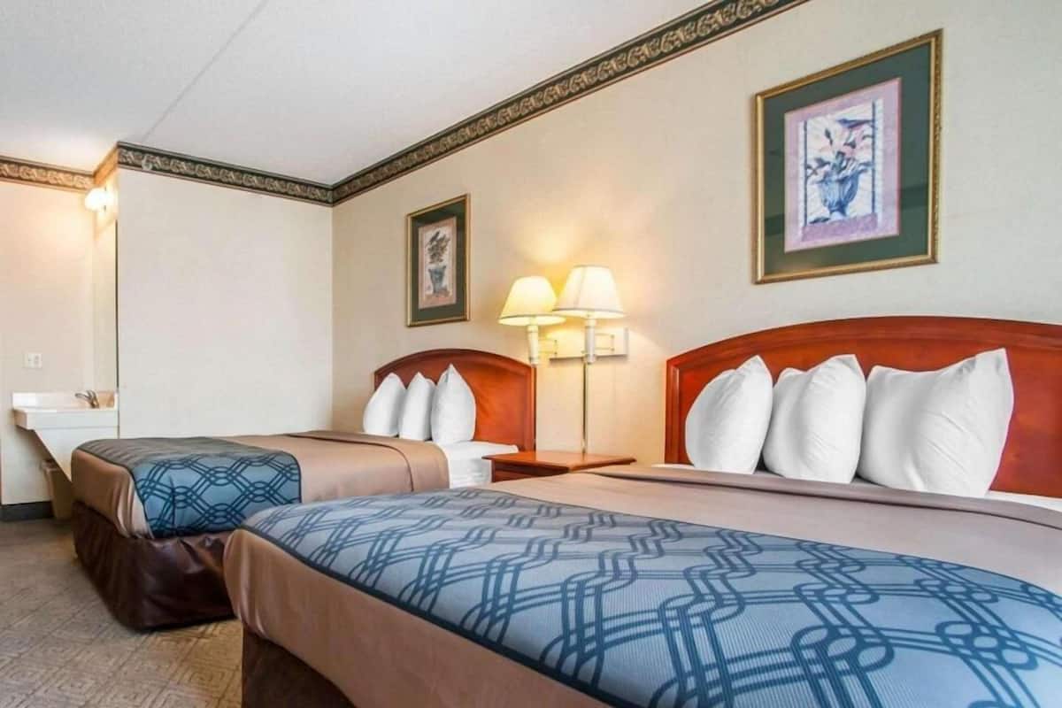 Une chambre d’hôtel avec deux lits, une table de chevet avec des lampes, un tableau encadré au mur et un petit lavabo.
