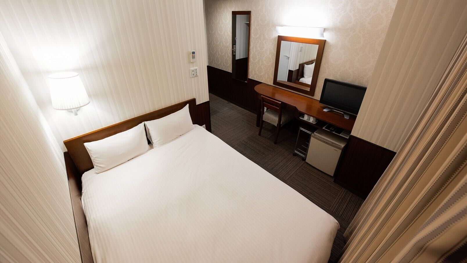 Una camera d'albergo con un letto, una scrivania, una televisione e uno specchio.