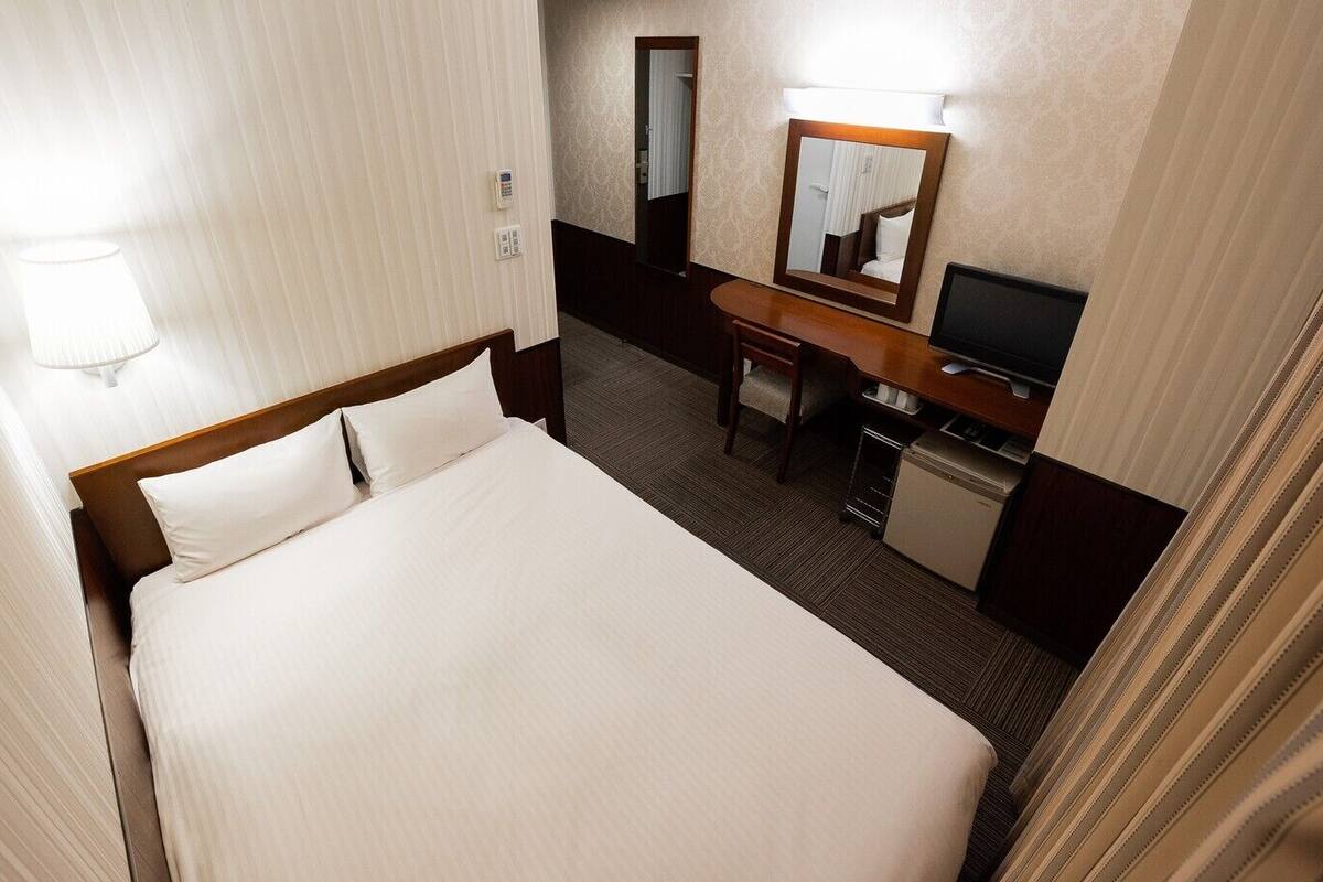 Ein Hotelzimmer mit Bett, Schreibtisch, Fernseher und Spiegel.