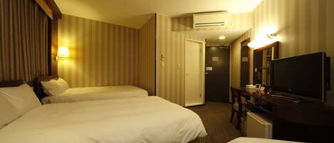 A hotel room with two beds, a desk, a television, and an air conditioning unit.