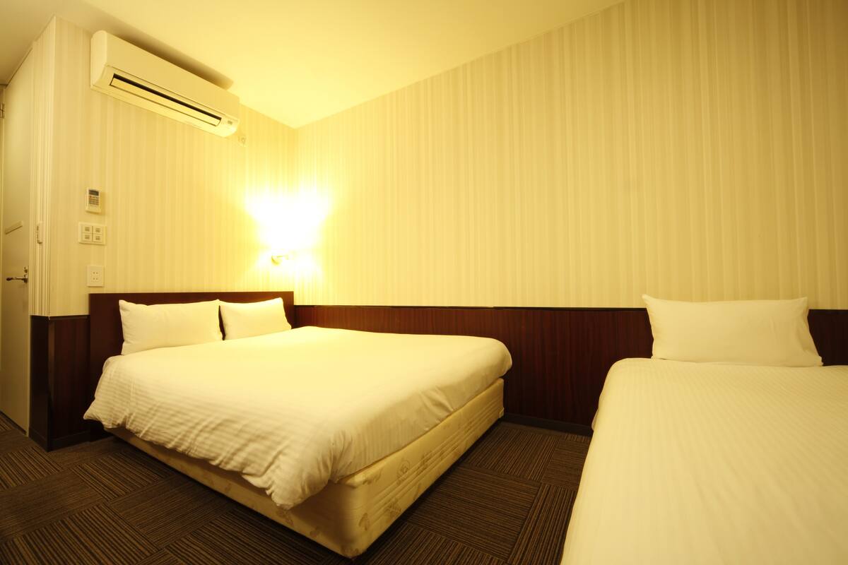 Ein Hotelzimmer mit zwei Betten, einer Wandklimaanlage und einer Nachttischlampe.