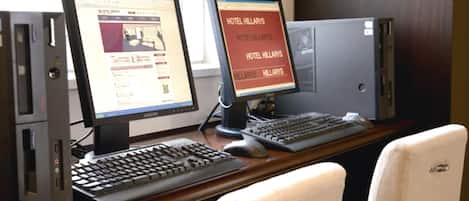 Two computer monitors on a desk with a keyboard and mouse, and a sign reading "HOTEL HILLARIES".
