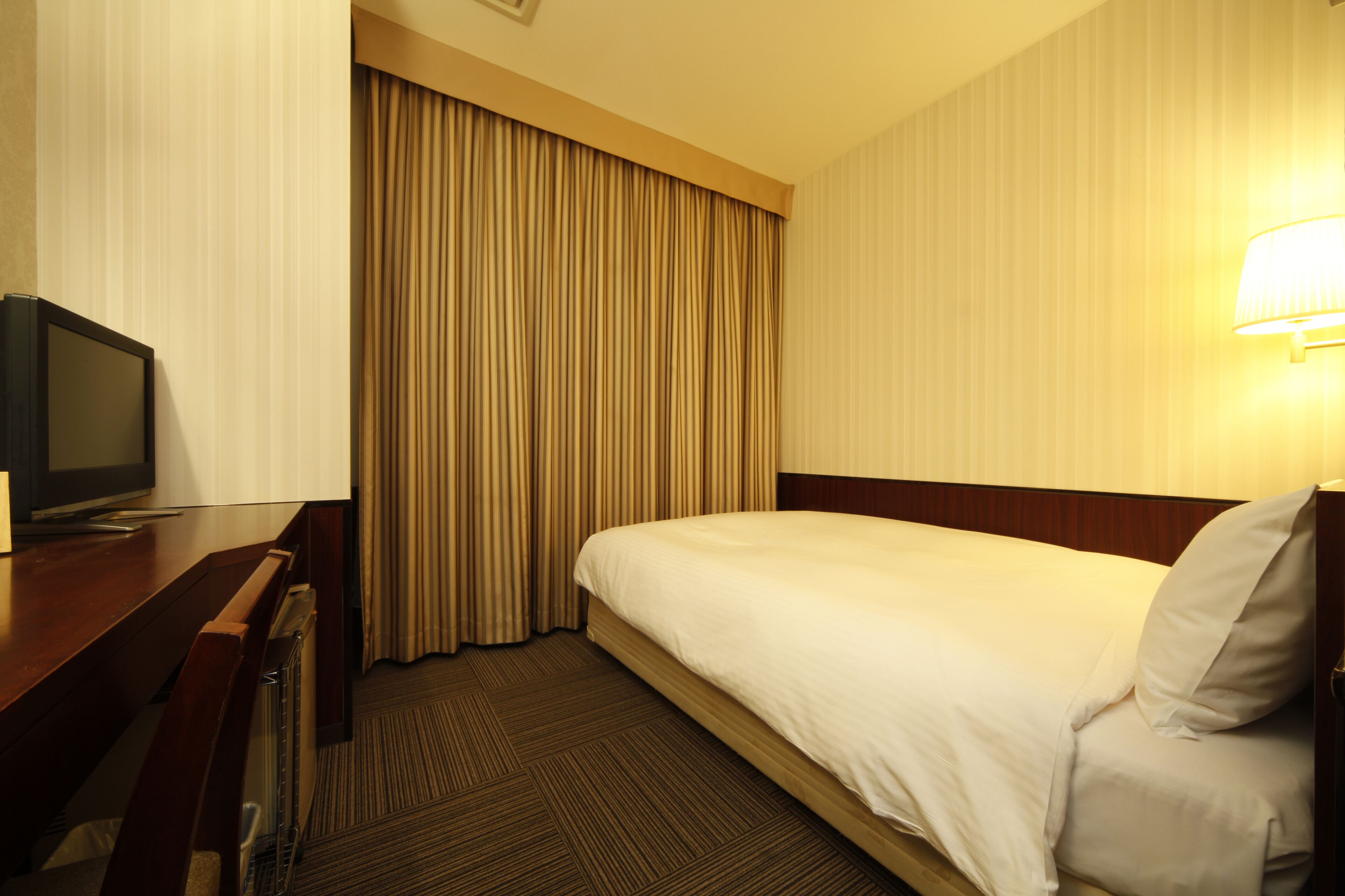 Une chambre d’hôtel avec un lit, un bureau avec une télévision et une lampe.