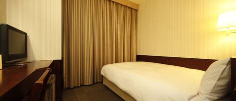 A hotel room with a bed, a desk with a television, and a lamp.