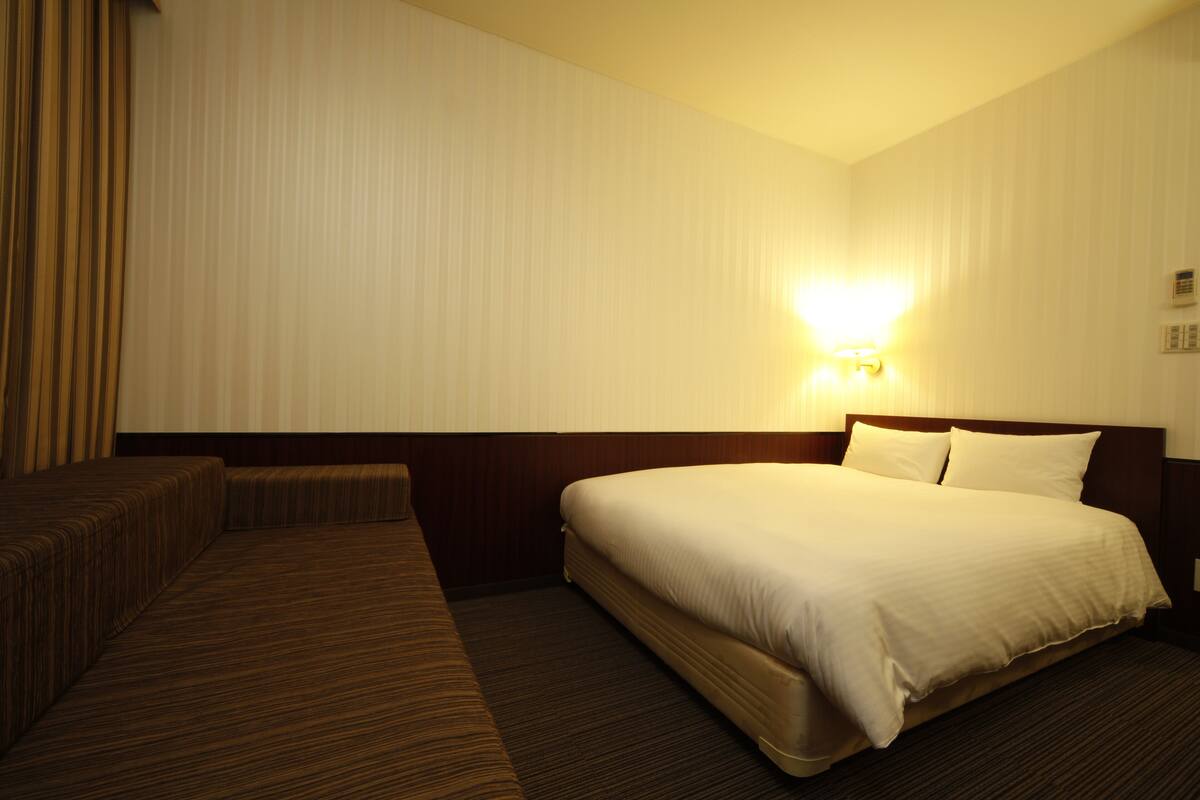 Ein Hotelzimmer mit einem großen Bett, einer kleinen Couch und einer Wandleuchte.