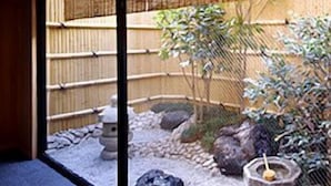 Un jardín japonés tradicional con un farol de piedra, una valla de bambú y un pequeño estanque.