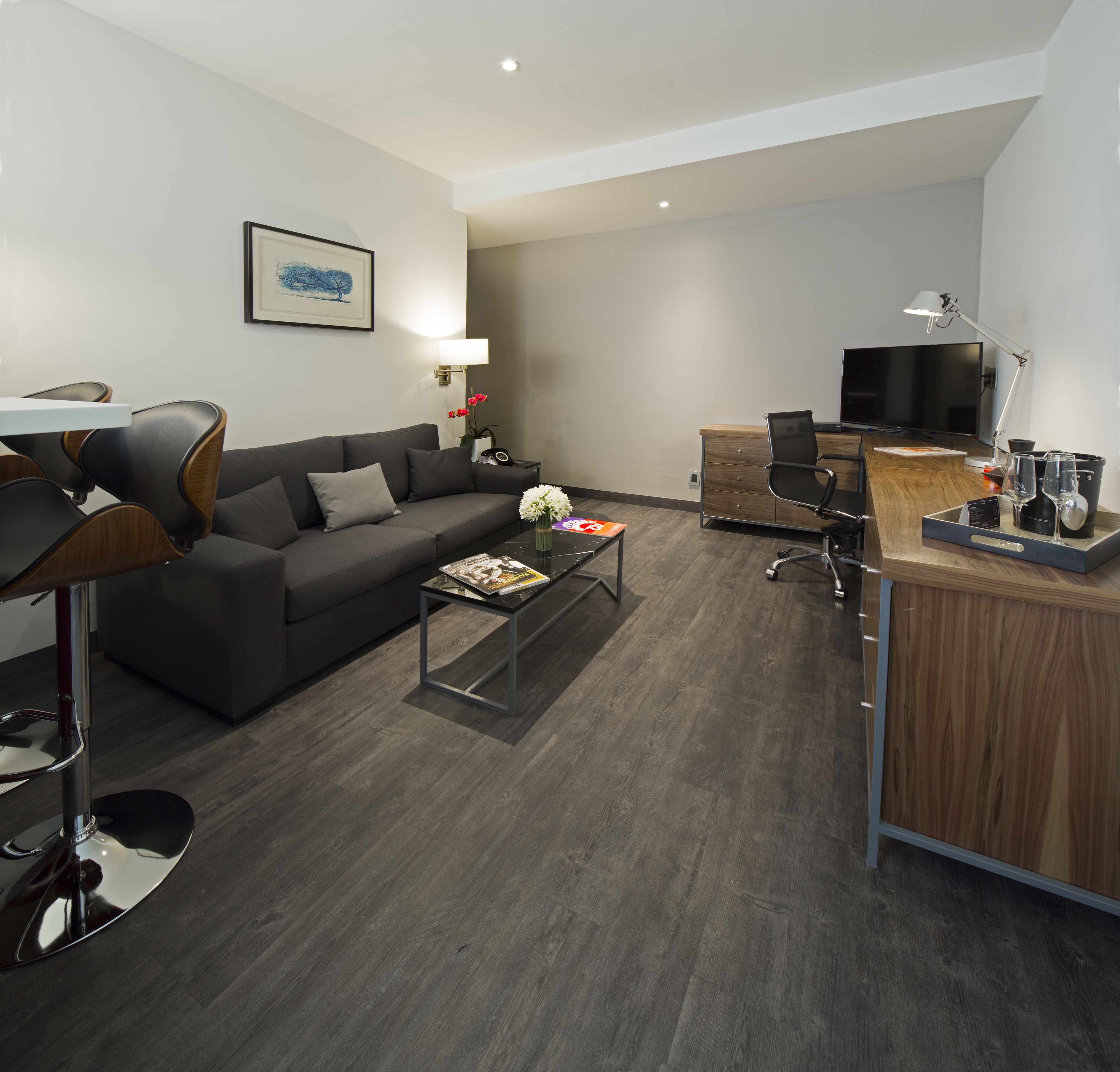 A modern living room with a grey sofa, a coffee table with magazines, a TV, and a desk with a computer and a lamp.
