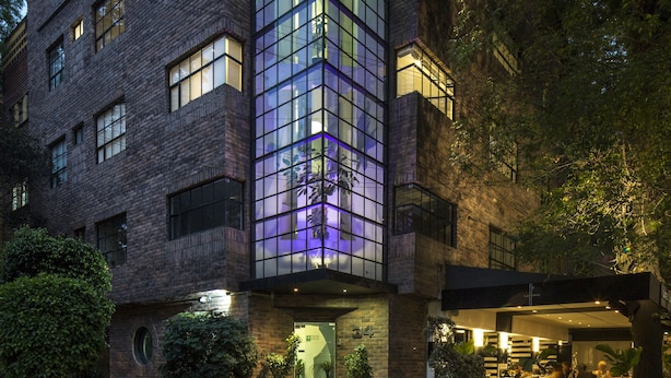 A modern building with a glass facade and brick exterior, featuring a central entrance and surrounding greenery. - FlowSuites Polanco (Mexico City)