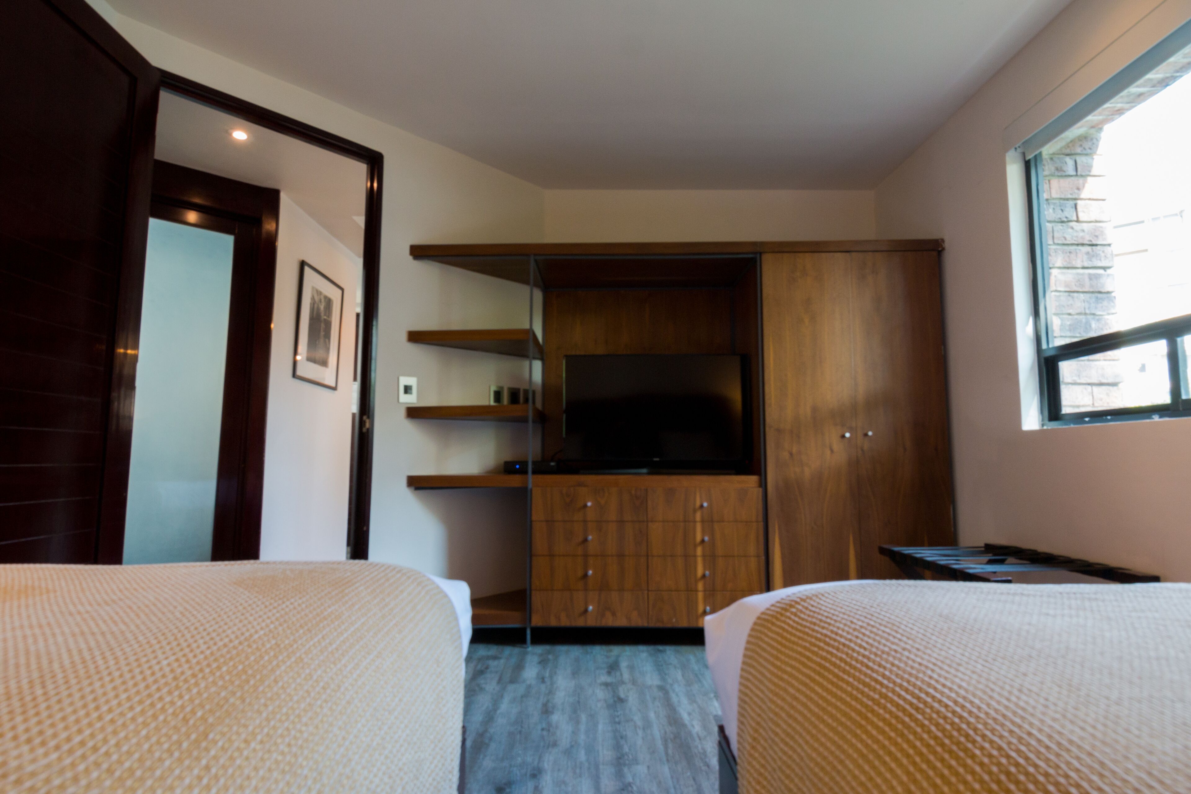 A hotel room with two beds, a wooden wardrobe, a television, and a window.
