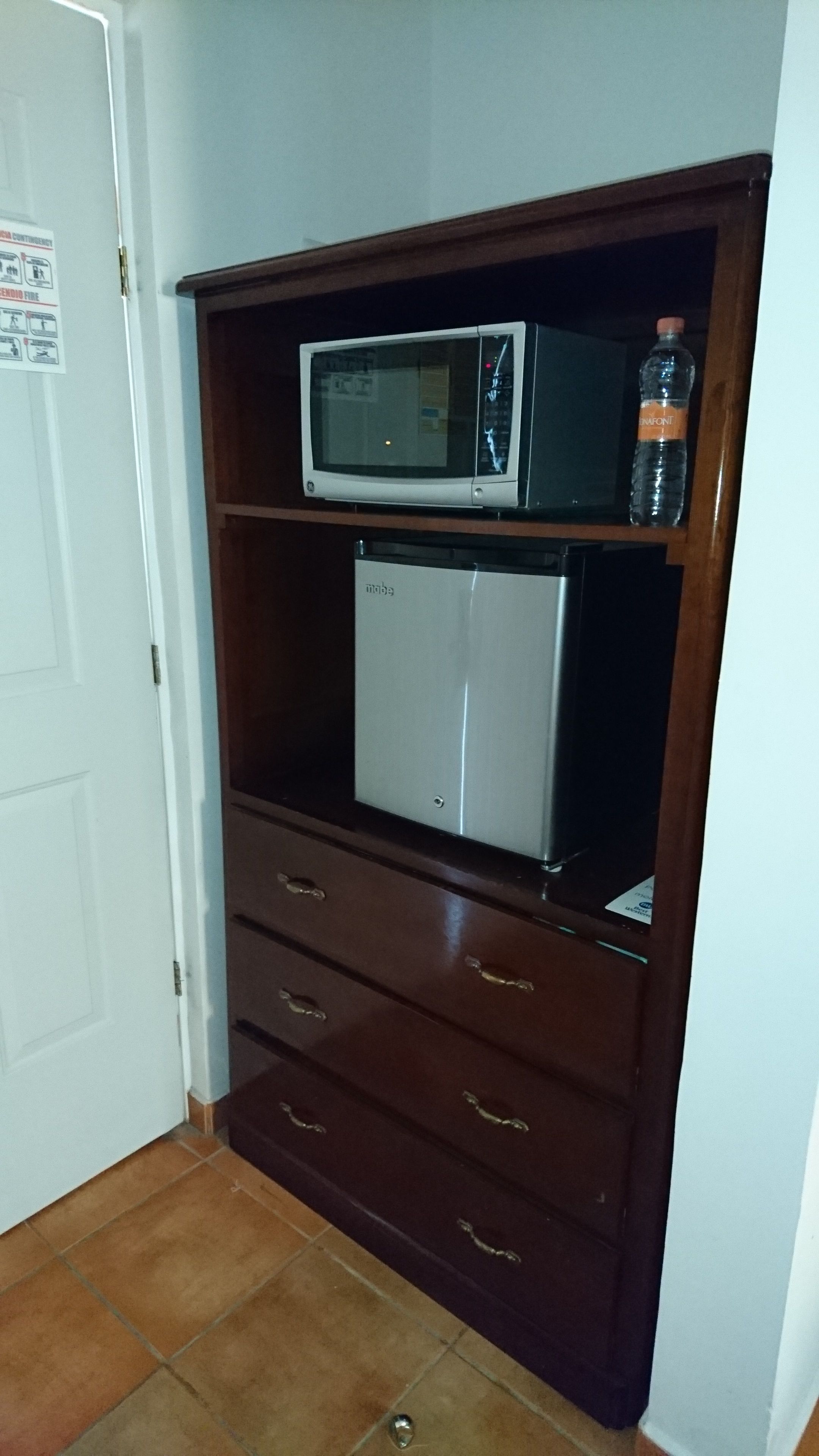 A kitchenette with a microwave, a mini-fridge, and a water bottle on a wooden cabinet.