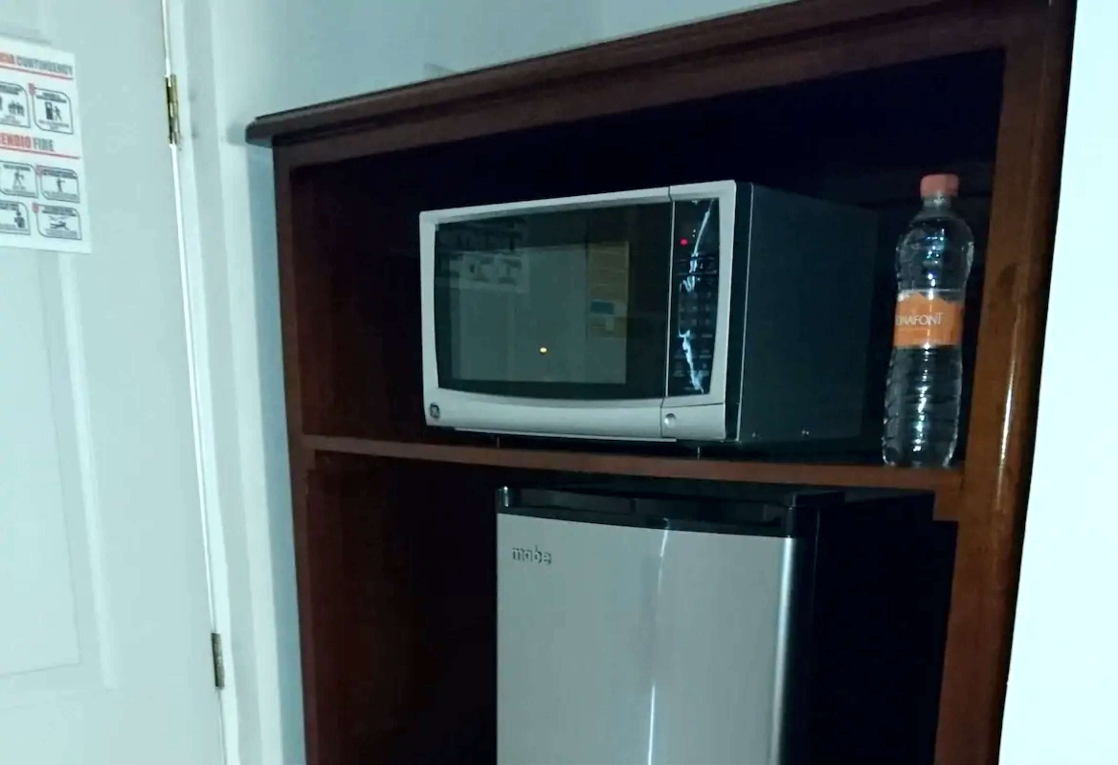 A microwave on a shelf above a mini fridge.