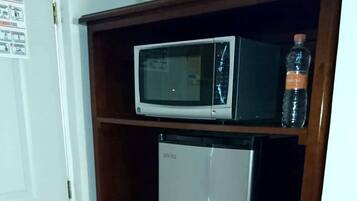 A microwave on a shelf above a mini fridge.