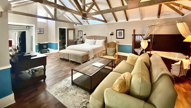 A spacious room with a high ceiling, a bed, a sofa, a coffee table, and a desk. - Coppersmith Inn B&B (Galveston)