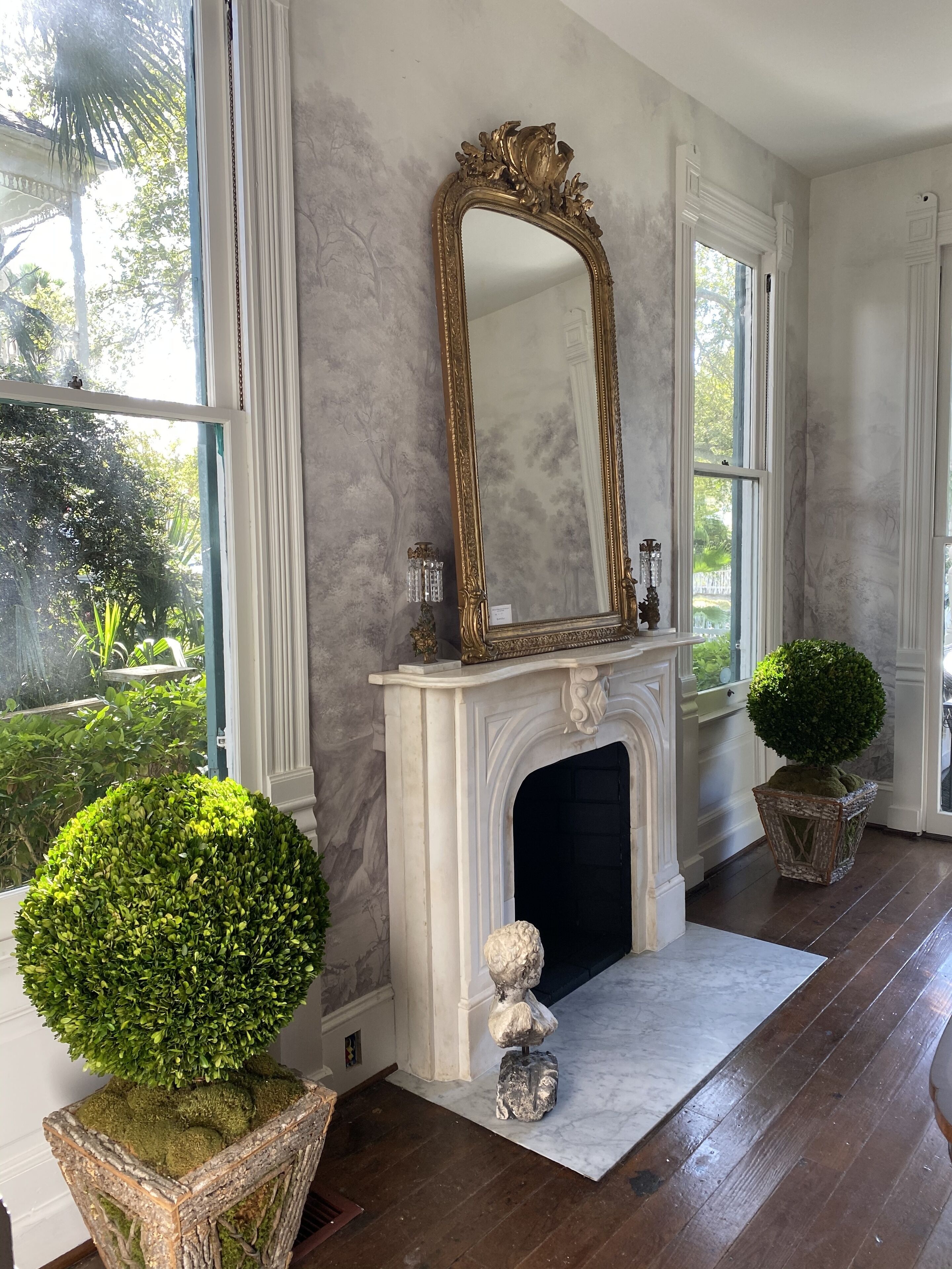 A room with a fireplace, a large mirror, and two potted plants.