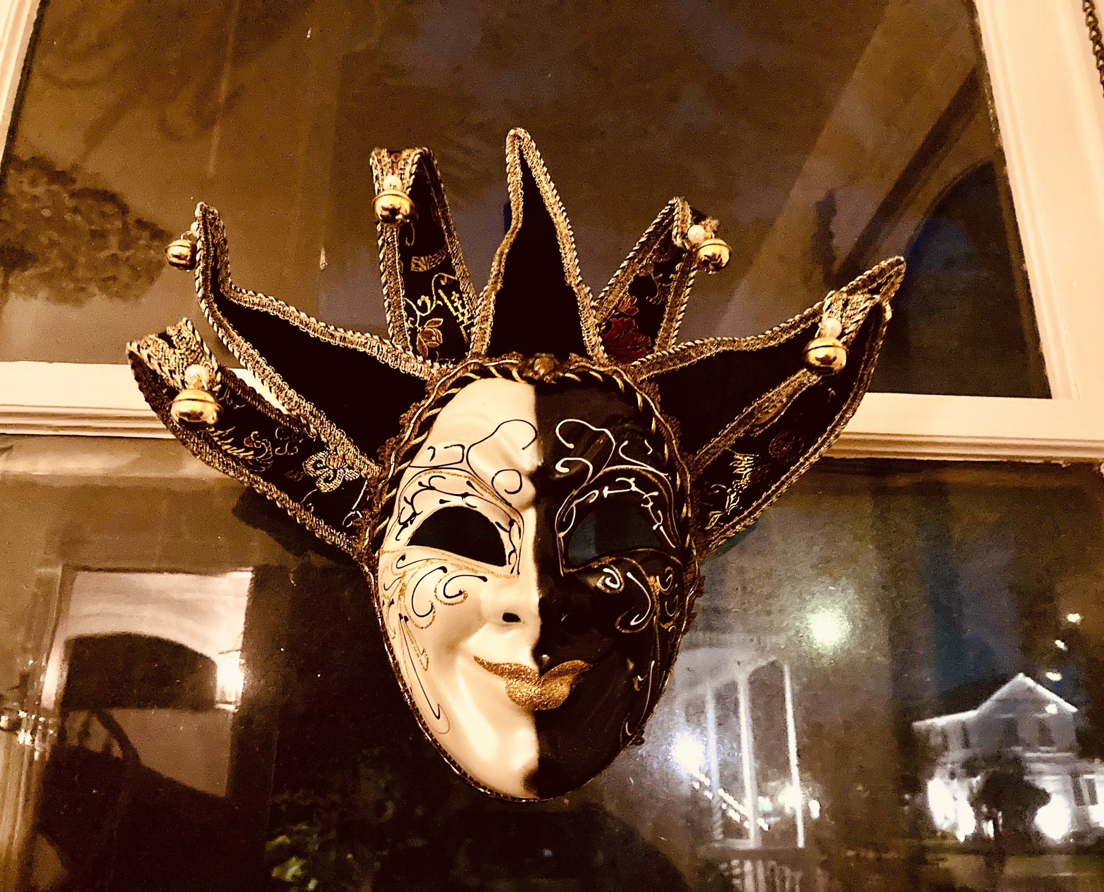 Máscara decorativa con diseños intrincados y un cascabel, exhibida frente a una ventana que refleja edificios.