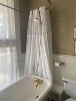 Un baño con bañera, cortina de ducha, inodoro y ventana con cortinas de encaje.