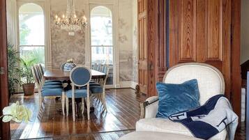 A spacious living room with a large white armchair, a dining area with blue chairs, and a chandelier.