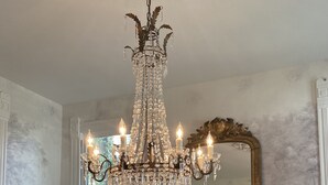 A dining room with a chandelier, a large mirror, and a vase of flowers on the table. - Coppersmith Inn B&B (Galveston)