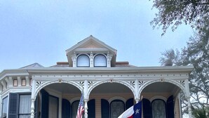 A two-story building with a balcony, a flag, and Mardi Gras decorations. - Coppersmith Inn B&B (Galveston)