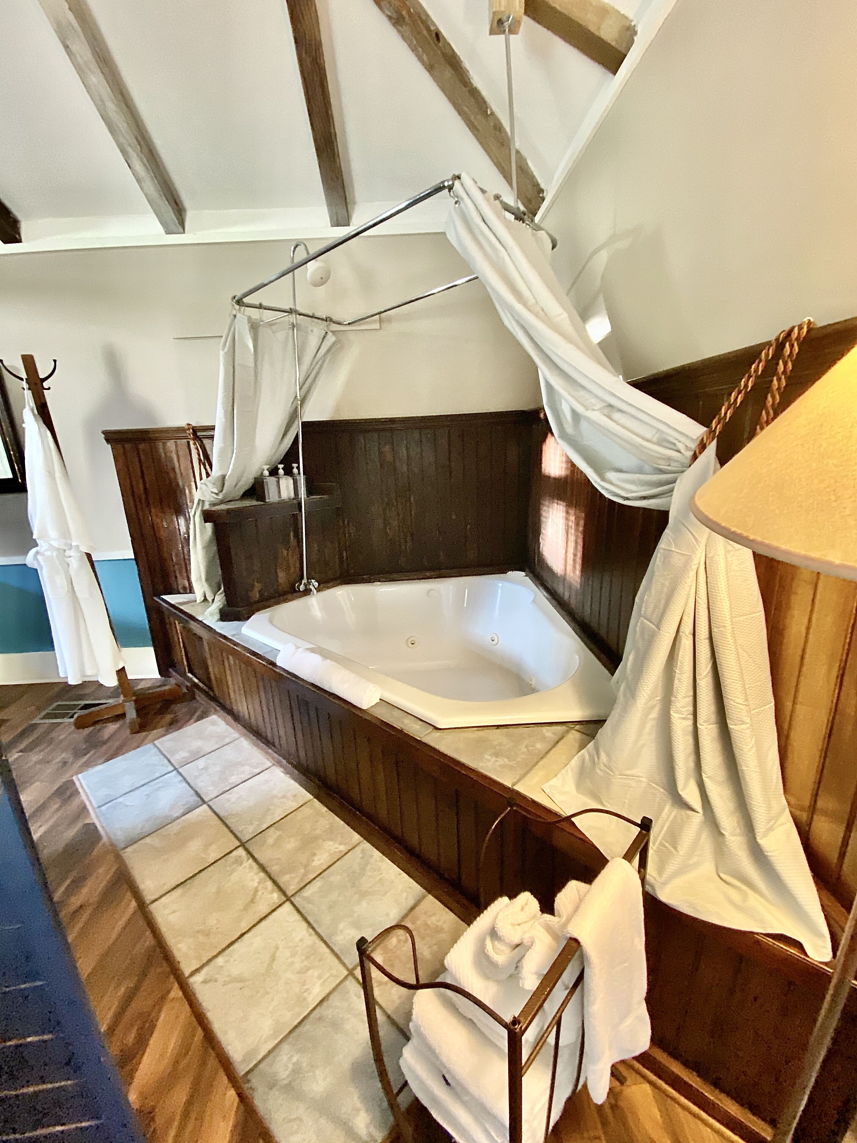 A room with a large bathtub, wooden paneling, a canopy, and a towel rack.