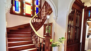 A wooden staircase with a curved design, leading to a landing with a potted plant and a table. - Coppersmith Inn B&B (Galveston)