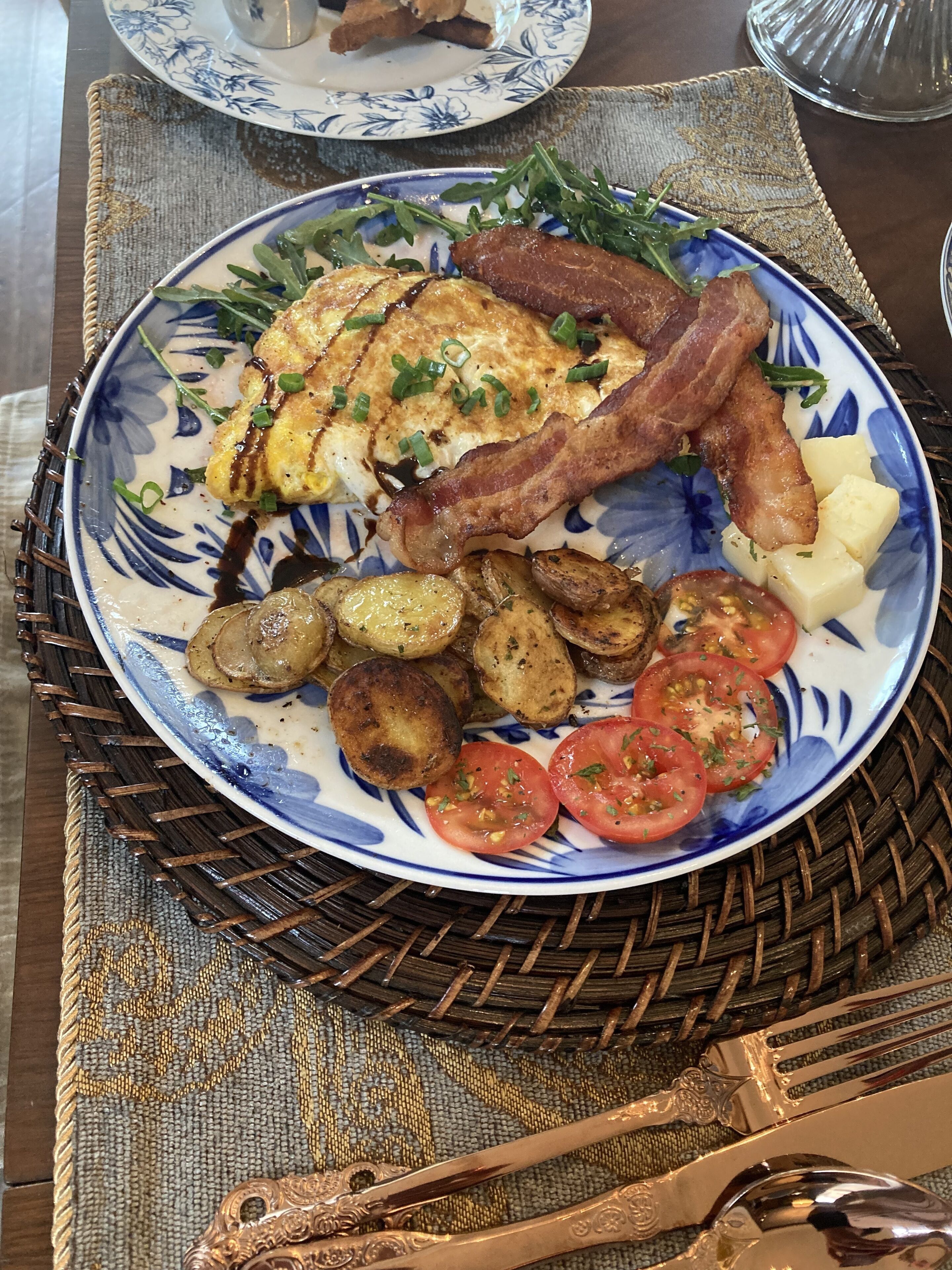 A plate of breakfast food including eggs, bacon, potatoes, and tomatoes on a blue and white patterned plate.
