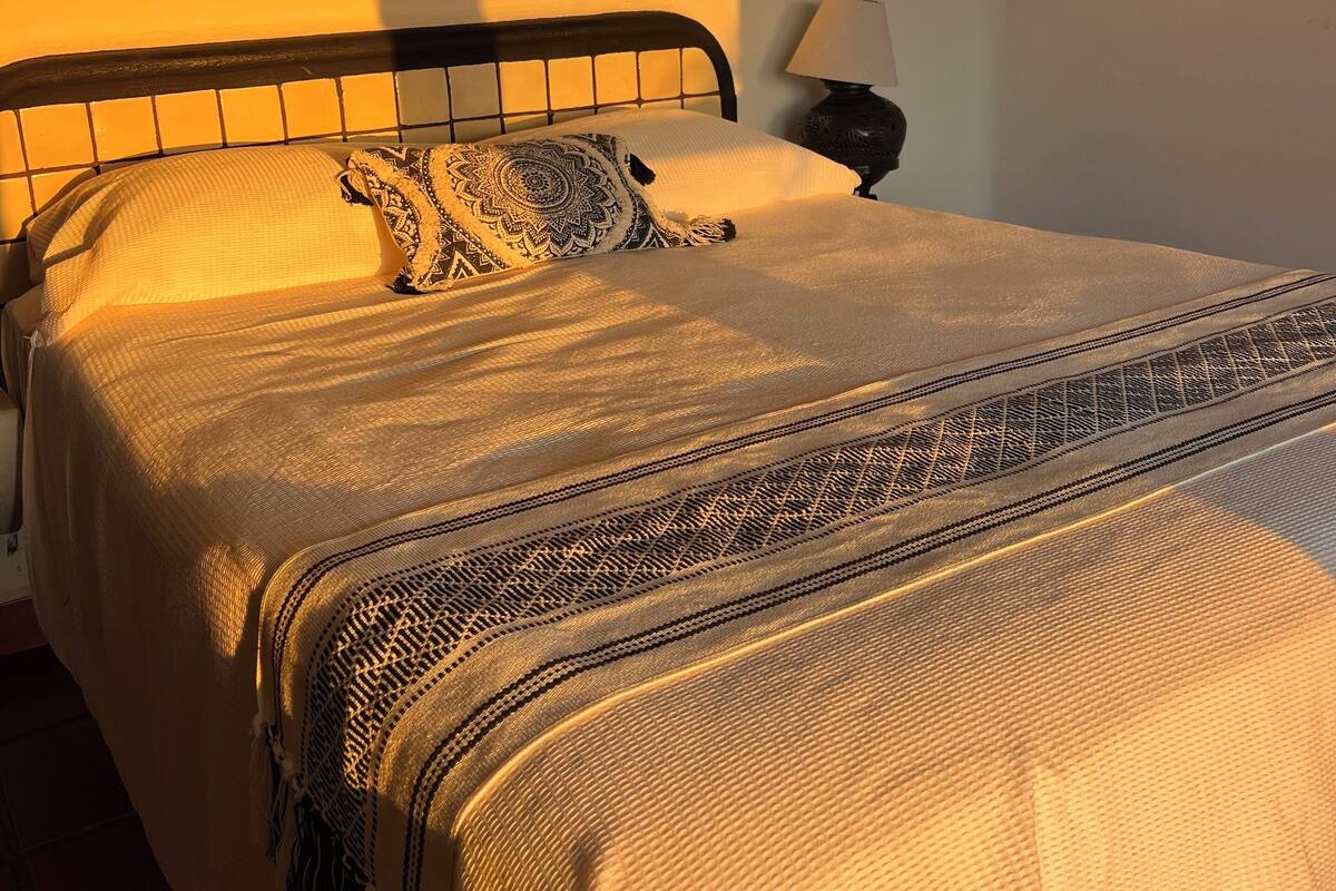 A bed with a patterned blanket, a bedside lamp, and a wall-mounted object.