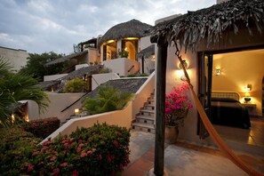 A hotel with a thatched-roof structure, a staircase leading to a bedroom, and a garden with pink flowers. - Agua Azul la Villa (Santa María Huatulco)