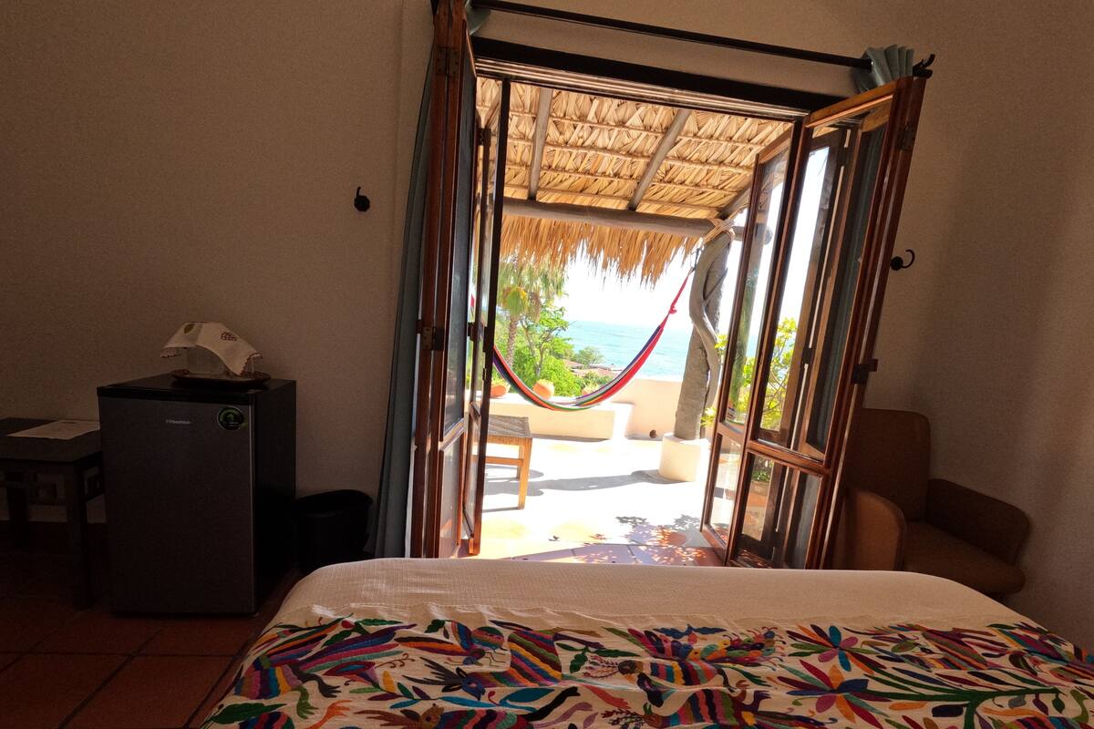 A room with a bed, a desk, and a view of the ocean through a glass door.