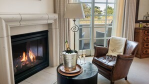 A cozy living room with a fireplace, a leather armchair, a coffee table with a champagne bucket, and a view of the outdoors through a large window. - Seal Cove Inn (Moss Beach)