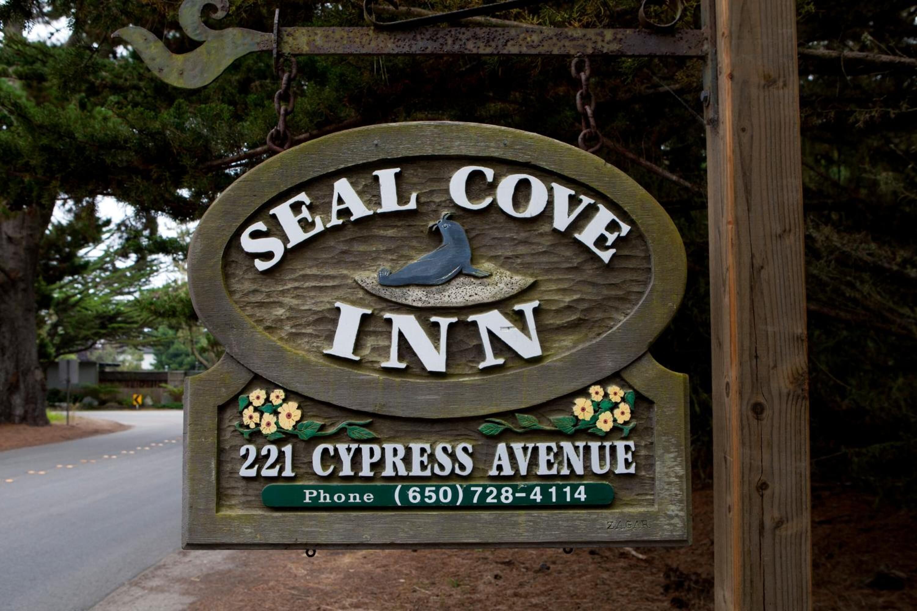 A wooden sign for Seal Cove Inn with a seal, flowers, and the address 221 Cypress Avenue.