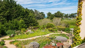 A garden patio with a wooden table and chairs, surrounded by various plants and trees. - Seal Cove Inn (Moss Beach)