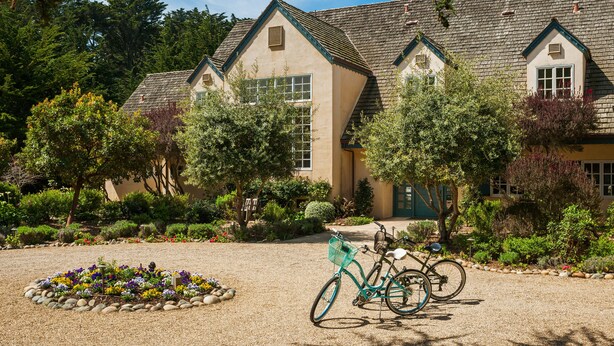 A building with a symmetrical facade, multiple windows, and a well-maintained garden with a gravel path and a bicycle. - Seal Cove Inn (Moss Beach)