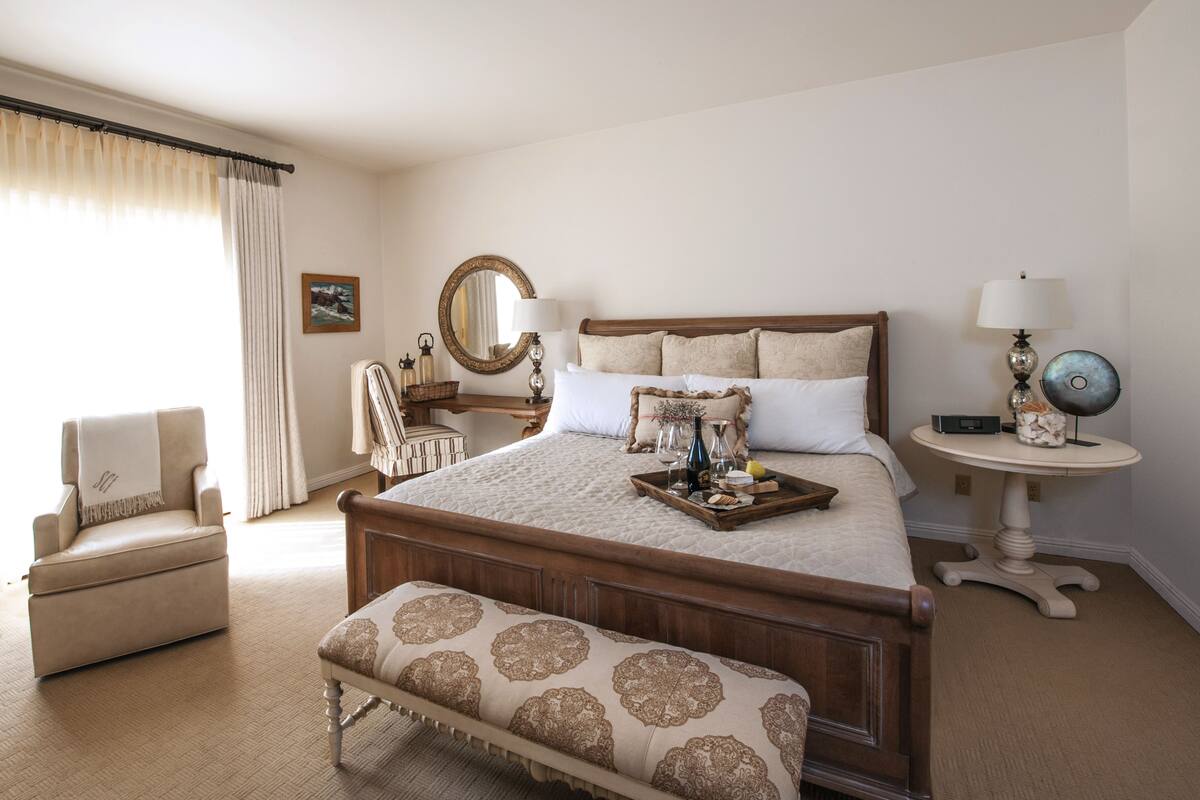 A neatly arranged bedroom with a large bed, bedside tables, a chair, and a bench.