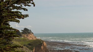 A coastal landscape with a sandy beach, clear blue water, and green vegetation. - Seal Cove Inn (Moss Beach)