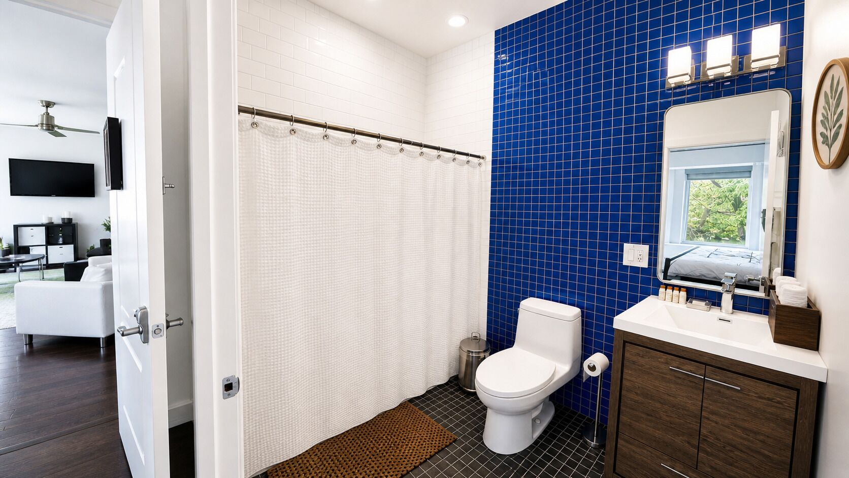 A bathroom with a white toilet, blue tiled walls, a shower curtain, a sink with a mirror, and a small trash can.