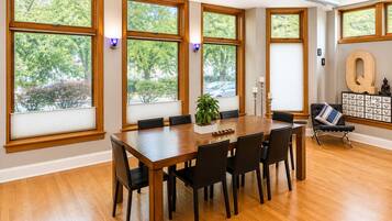 Un comedor con una mesa de madera, sillas y ventanas amplias con persianas.