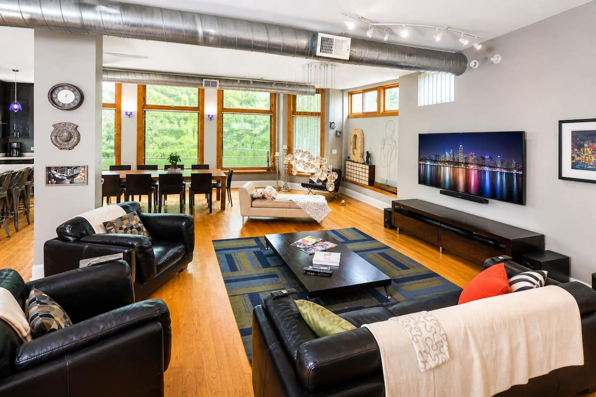 A modern living room with leather sofas, a coffee table, a TV, and a dining area with natural light.