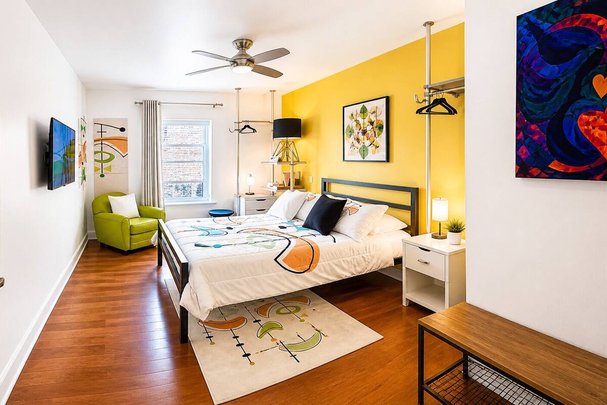A bedroom with a bed, bedside tables, a chair, a ceiling fan, and artwork on the walls.