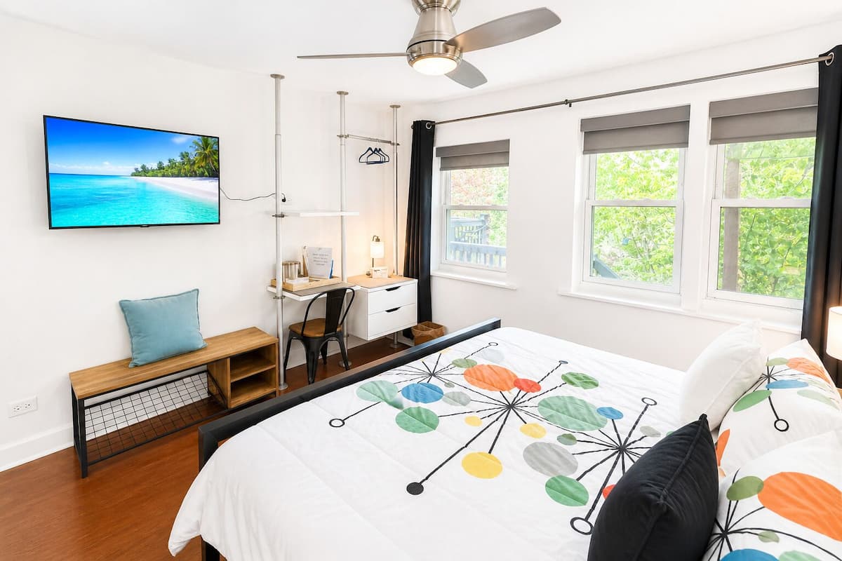A bedroom with a bed, desk, chair, and a TV on the wall.