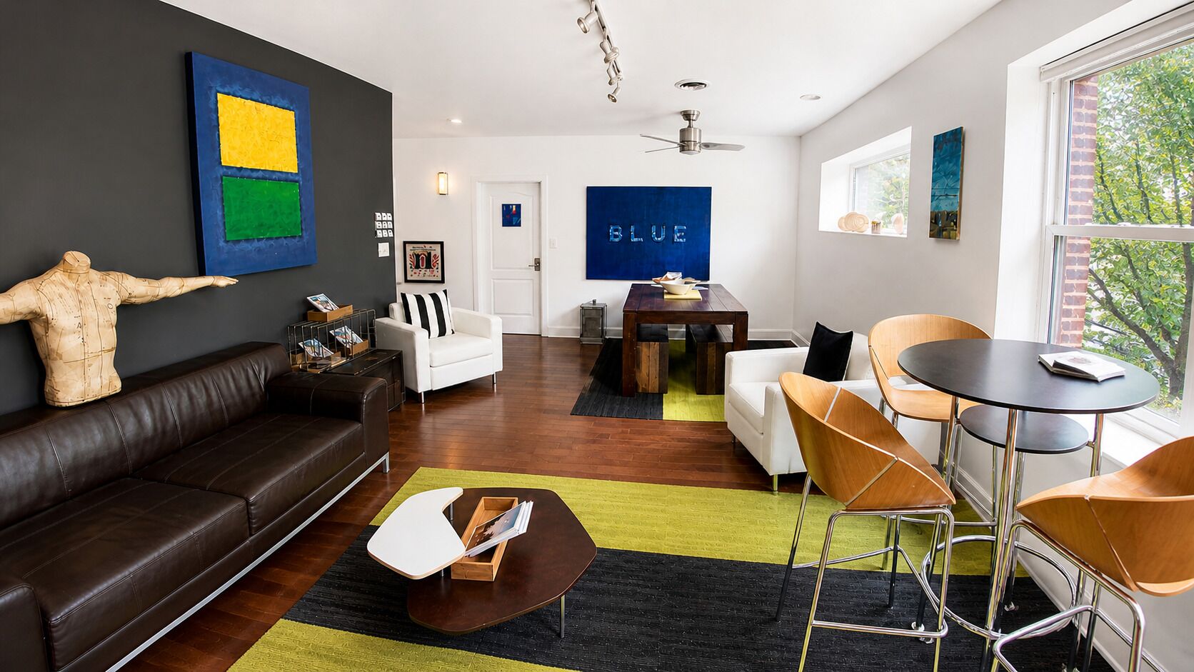 A modern living room with a dark brown sofa, a white armchair, a wooden coffee table, and a dining area with a table and chairs.